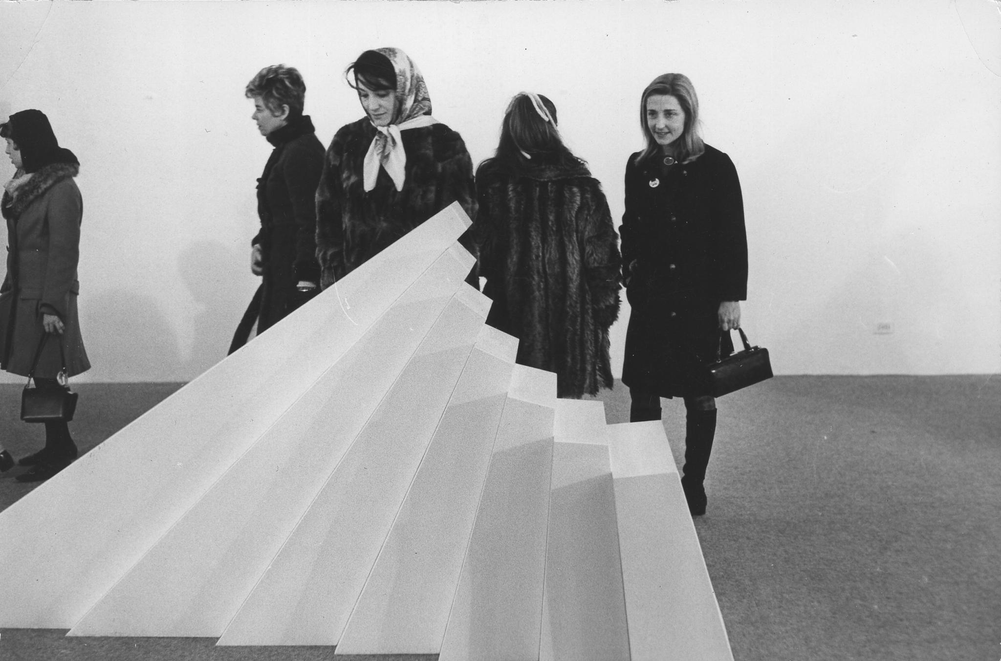 a large white geometric sculpture installed in a gallery with people looking at it