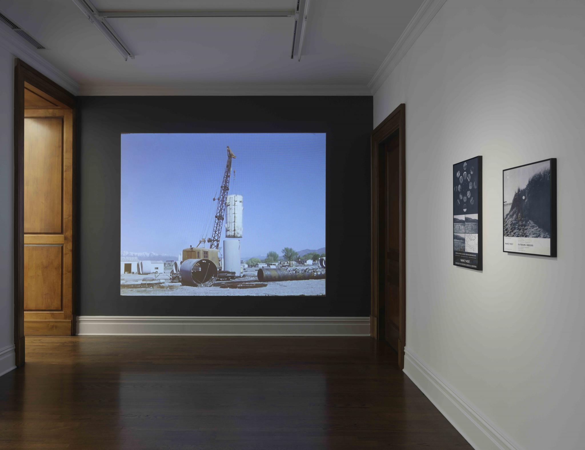 a film projected in a gallery, with two black and white posters 