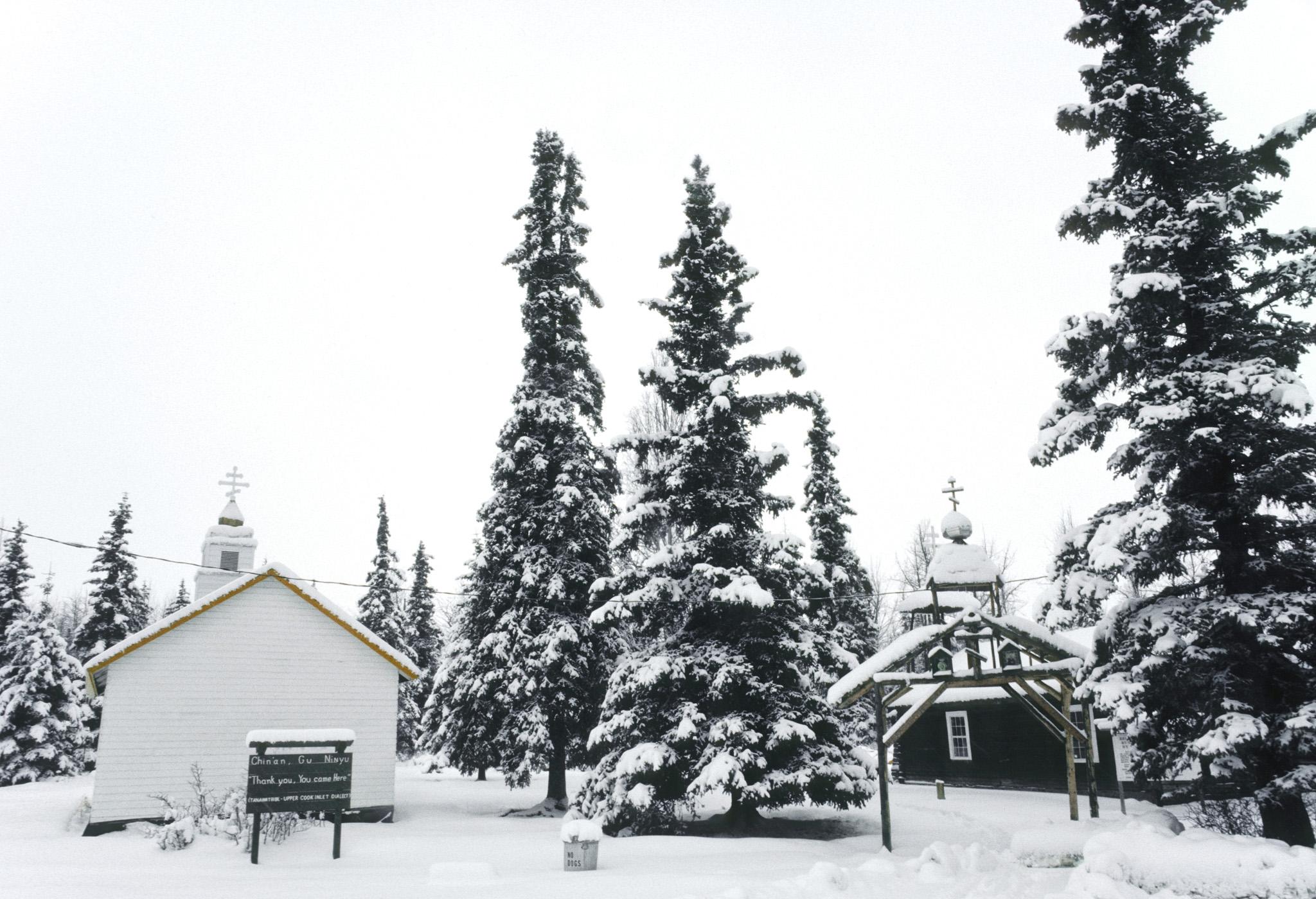 a snowy graveyard with large house-like structures as gravemarkers