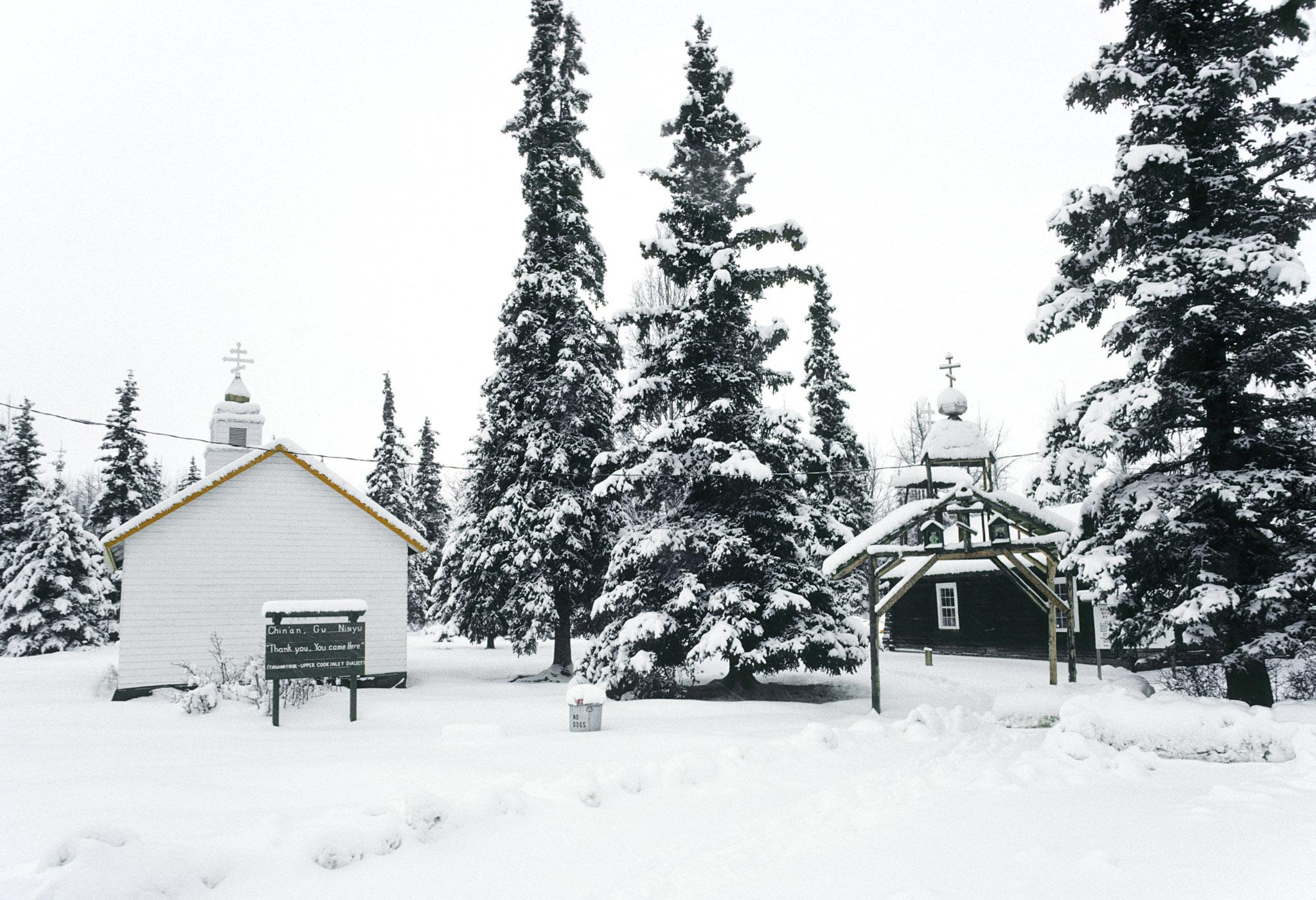 a snowy graveyard with large house-like structures as gravemarkers