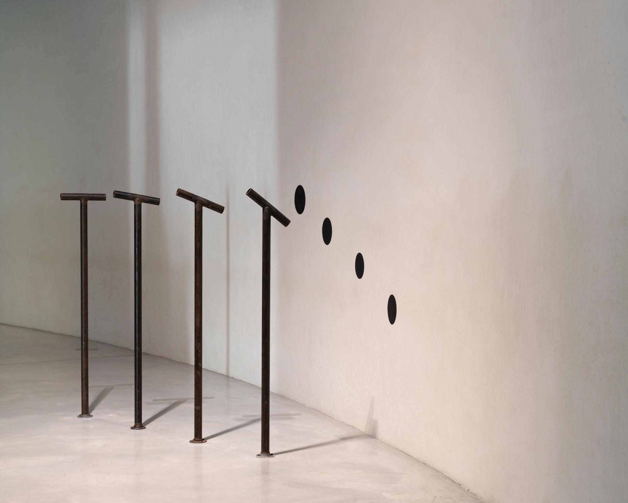 four steel pipes extend up from the floor with viewing pipes pointed at four black circles on the wall