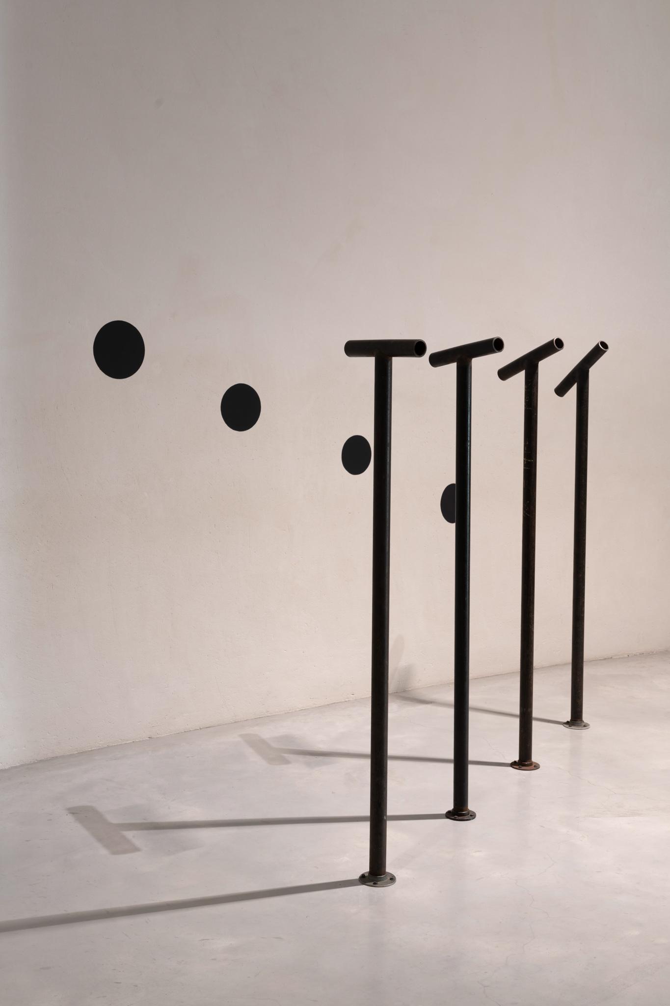 four steel pipes extend up from the floor with viewing pipes pointed at four black circles on the wall