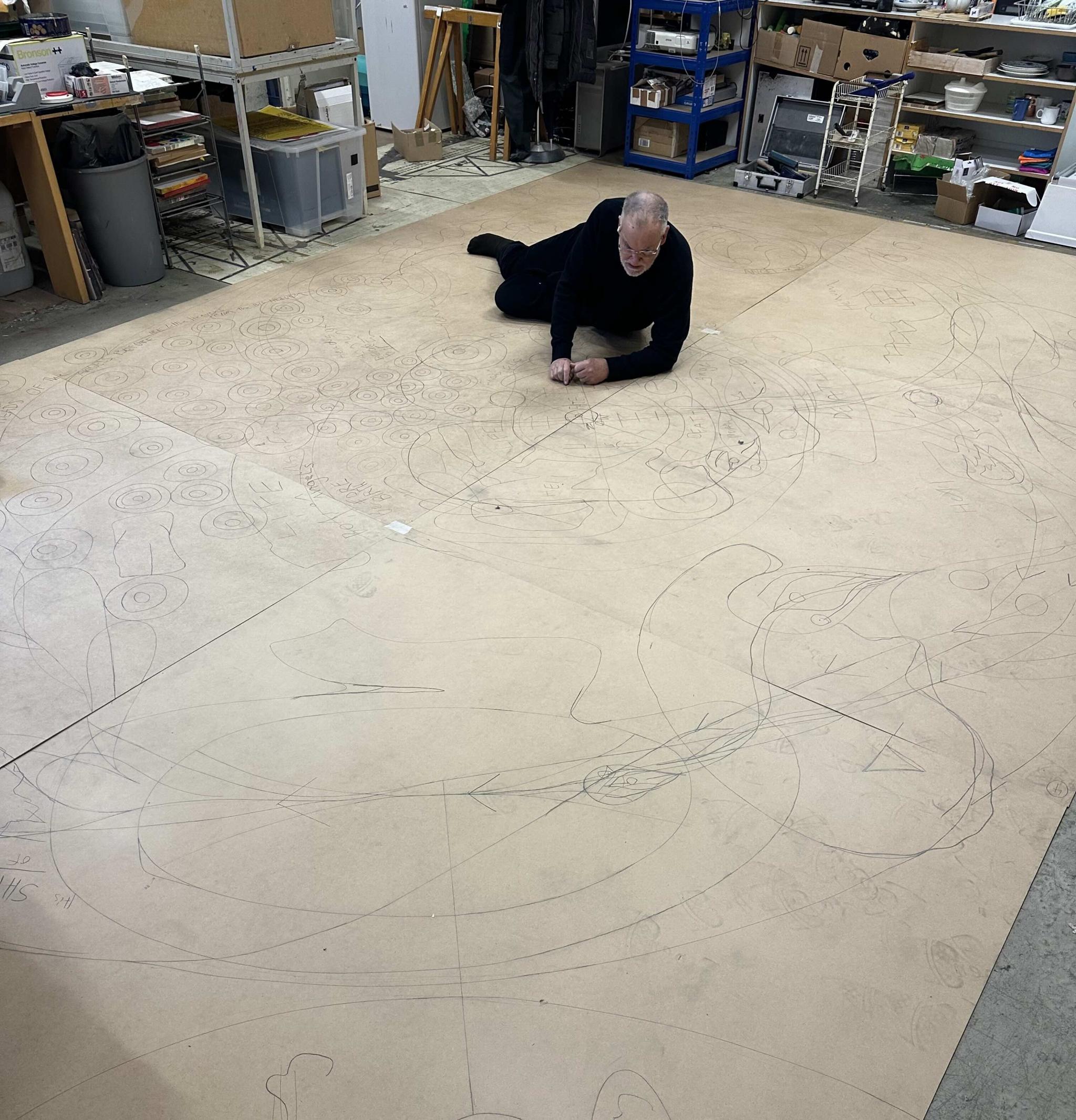 an artist drawing on a large sheet of paper, lying down