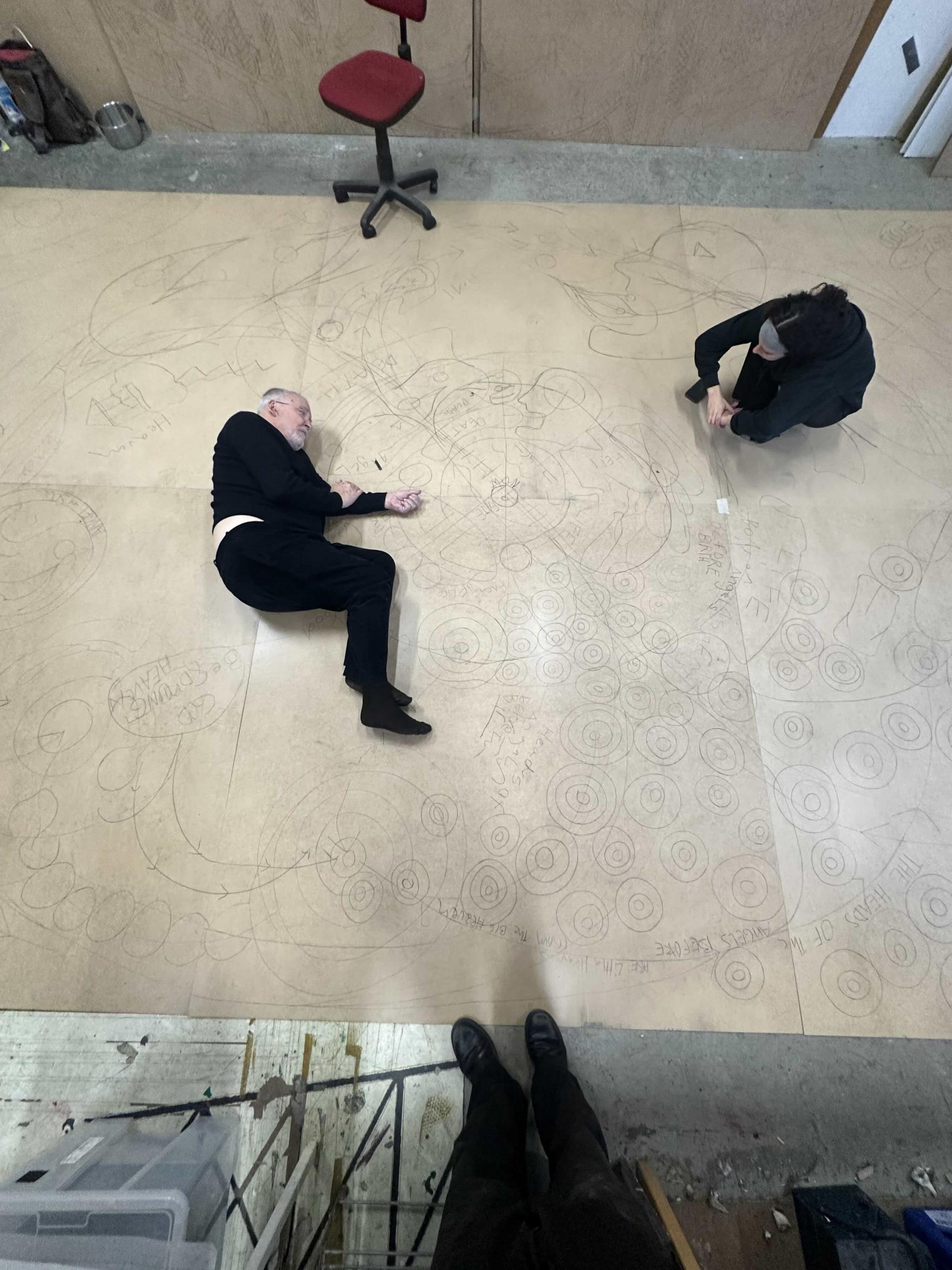 an artist drawing on a large sheet of paper, lying down