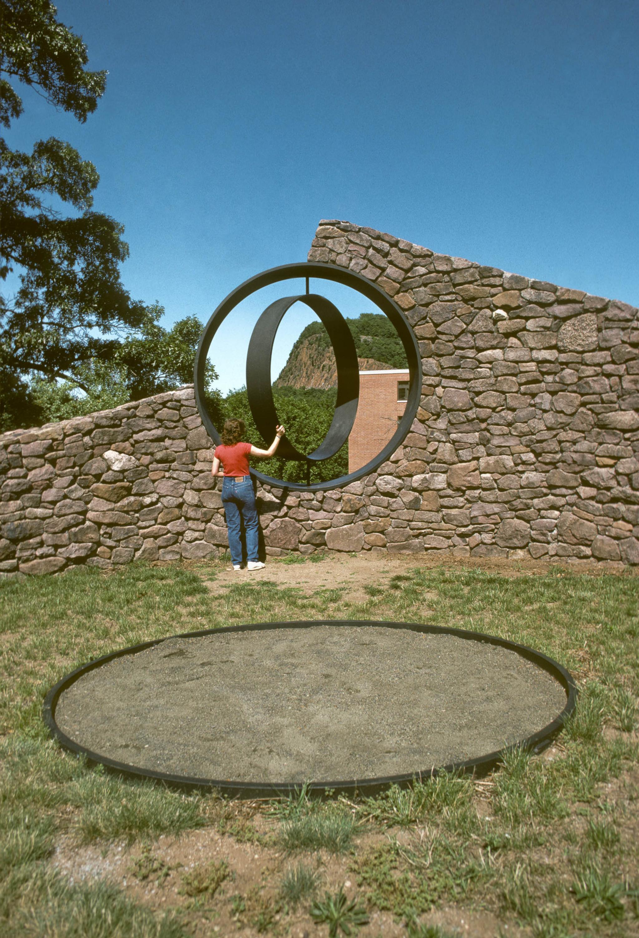 a sculpture made of a curved stone wall with a viewing circle within it