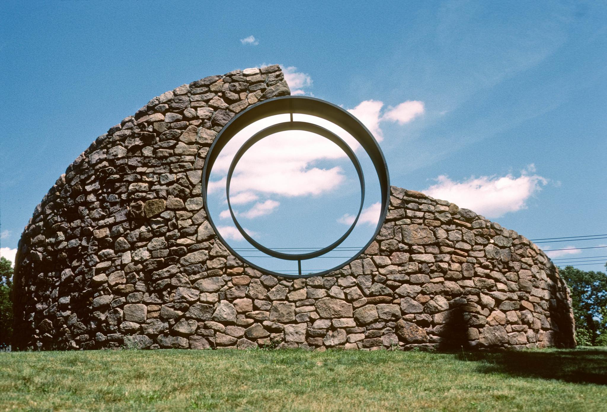 a sculpture made of a curved stone wall with a viewing circle within it