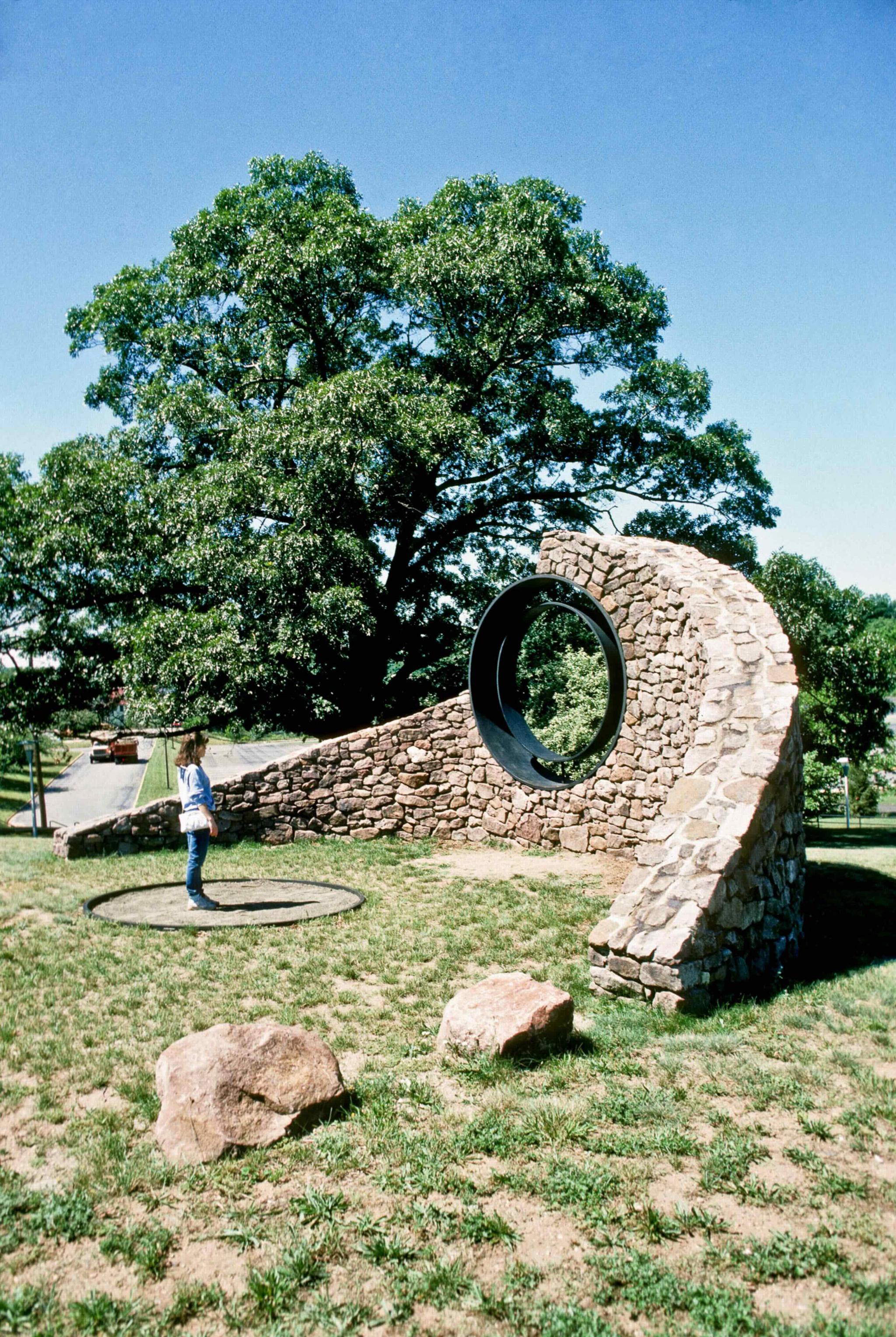 a sculpture made of a curved stone wall with a viewing circle within it